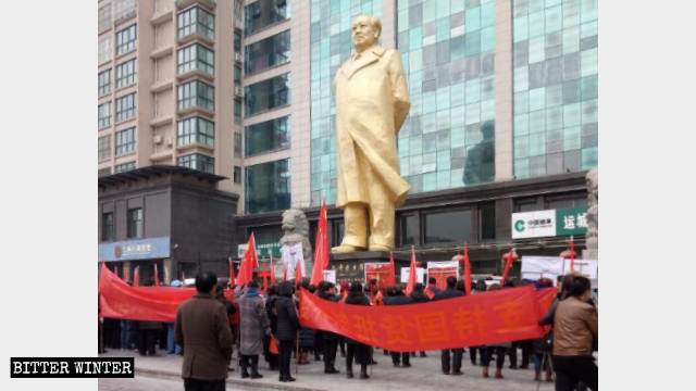 Un grupo de manifestantes se reúne bajo una gran estatua de bronce de Mao Zedong