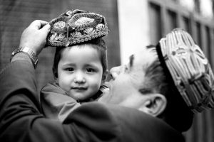 Un hombre le coloca un doppa bordado a su hijo