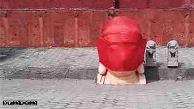 La cabeza de una estatua de Buda demolida está envuelta con un paño rojo
