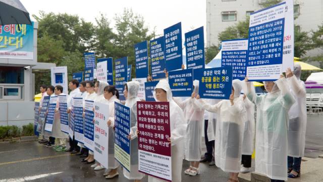 Miembros de la IDT sostienen letreros en la entrada de las instalaciones de la IDT en Onsu, protestando contra el PCCh por utilizar a sus familiares para realizar manifestaciones falsas.