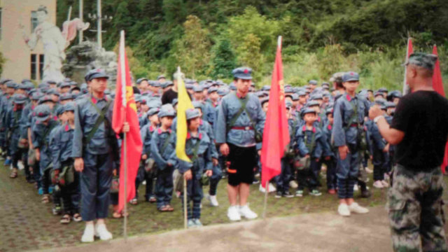 Estudiantes con uniformes del Ejército Rojo llevan mochilas en las que están impresos un retrato del presidente Mao y la consigna "Servir al pueblo".