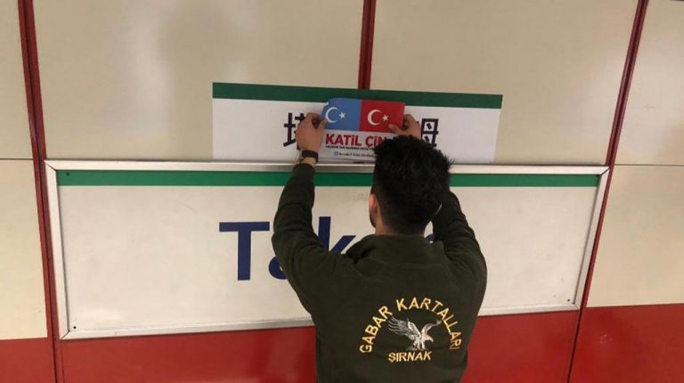 Un simpatizante turco de la causa uigur cubre el letrero en mandarín de la parada Taksim del tranvía con las banderas de Turquestán Oriental y Turquía y las palabras "katil çin", las cuales significan "Gobierno chino asesino".
