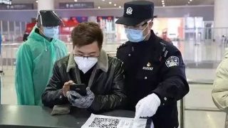 Los agentes de policía de un puesto de control situado en la estación ferroviaria este de Hangzhou les dan instrucciones a los pasajeros para que utilicen sus teléfonos móviles para escanear los códigos de salud.