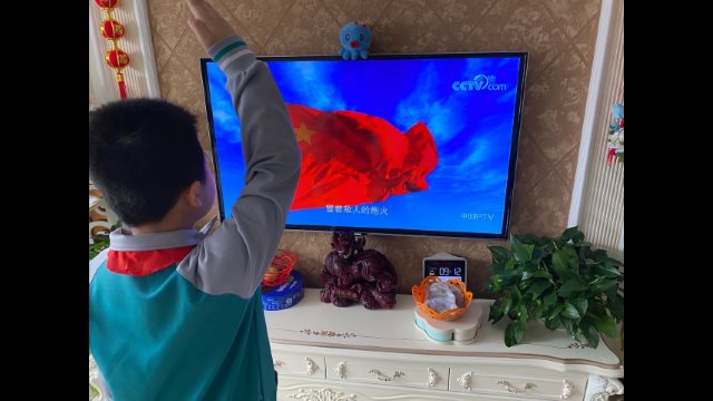 Un estudiante de primaria hace el saludo militar mientras mira en su hogar emplazado en la ciudad de Jiaozhou de Shandong una ceremonia de izamiento de la bandera durante una clase en línea impartida por televisión